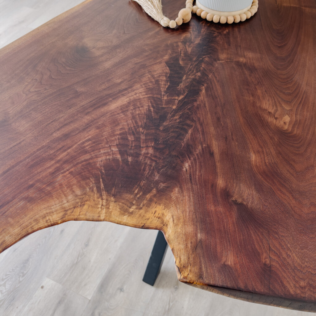 Close-up of a wooden table featuring rich, natural grain patterns and an irregular live edge, embodying the latest furniture trends. The surface has a warm, polished finish. A decorative piece with small wooden beads and part of a white vase is partially visible on the table. Close-up of a wooden table featuring rich, natural grain patterns and an irregular live edge, embodying the latest furniture trends. The surface has a warm, polished finish. A decorative piece with small wooden beads and part of a white vase is partially visible on the table.