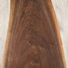 The "Ready To Ship - Black Walnut Live Edge Coffee Table," crafted from rich Black Walnut, boasts a polished, dark surface with natural grain patterns and curves. Set against a light wood floor, the intricate swirls and live edge waves of the wood grain are prominently visible, creating a striking visual contrast with the lighter floor beneath.