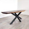 The Ready To Ship - Black Walnut Live Edge Coffee Table, featuring dark, angled metal legs and a natural, rustic aesthetic, is positioned on a light-colored wooden floor against a plain white wall.