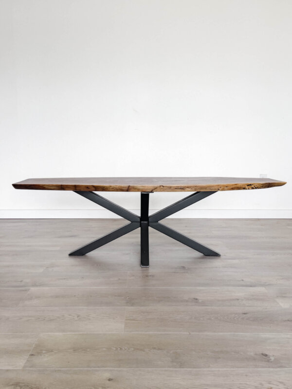 Introducing the Ready To Ship - Black Walnut Live Edge Coffee Table: a minimalist design crafted from rich black walnut wood and featuring black crisscross metal legs. This elegant piece is ready to ship and rests beautifully on a light gray hardwood floor against a plain white wall.