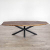 The "Ready To Ship - Black Walnut Live Edge Coffee Table" stands elegantly on a gray floor, featuring a top crafted from black walnut with an irregular, natural shape. Its sleek metal base with crossed legs adds a modern and rustic aesthetic. Set against a plain white background, this striking piece is prepared for immediate shipping.