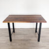 The Ready To Ship - Black Walnut Desk With H-Shaped Legs features a rectangular design with a wooden top and four H-shaped, black metal legs. It stands on a light-colored hardwood floor against a plain white wall. Featuring a smooth finish with distinct wood grain patterns, this elegant piece is ready to ship.