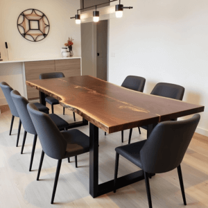 A modern dining room features a live edge wooden table with black metal legs, surrounded by six dark gray upholstered chairs. A minimalist light fixture hangs above, and a wall with a decorative mirror and vase adds a touch of elegance.