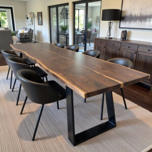 In a modern dining room, a remarkable Black Walnut Book Matched Dining Table with black metal legs takes center stage. It is surrounded by eight elegant black chairs. The decor includes a spacious sideboard, minimal artwork, and a black floor lamp, all enhanced by the beautifully diffused natural light throughout the space.